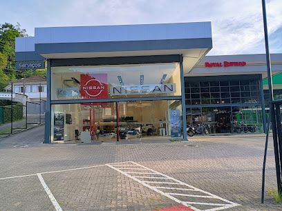 Fachada da concessionária Nissan com janelas de vidro e estacionamento em frente.