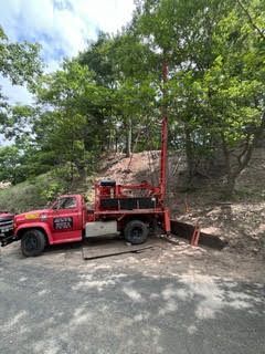 Red drilling rig truck on a dirt road by trees.