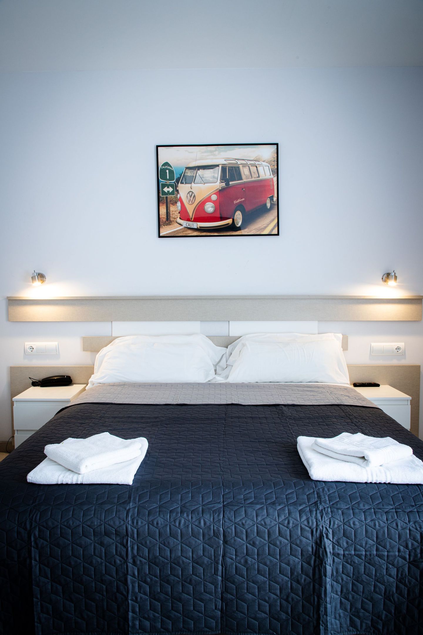 Habitación de hotel con cama de edredón oscuro y lámina enmarcada de furgoneta VW roja sobre la cama.
Ask ChatGPT
