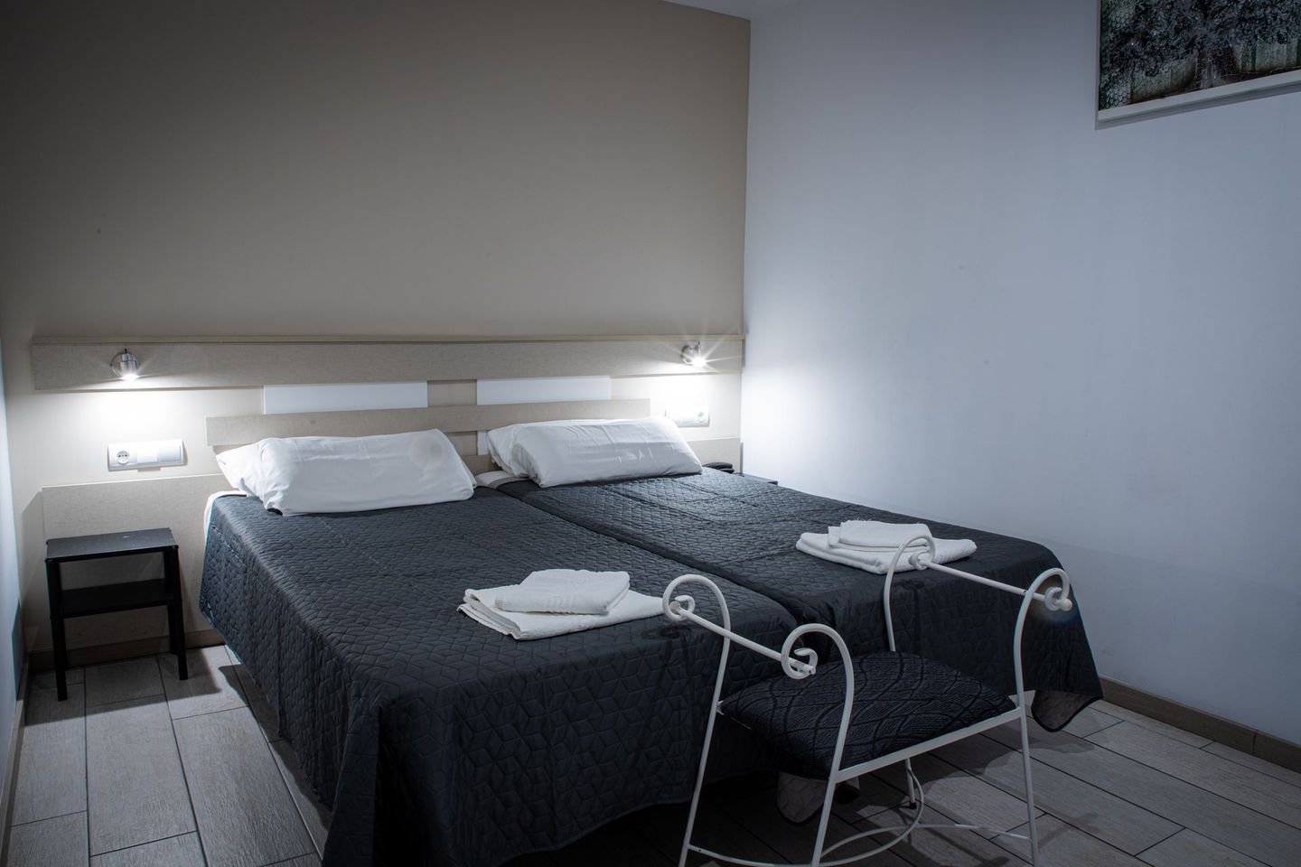 Una habitación de hotel con dos camas individuales con colchas grises, almohadas blancas y una silla blanca.