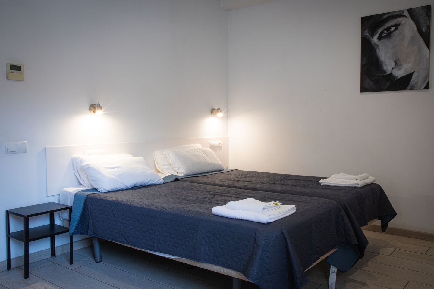 Una habitación de hotel con dos camas individuales, paredes blancas y un cuadro de una persona.