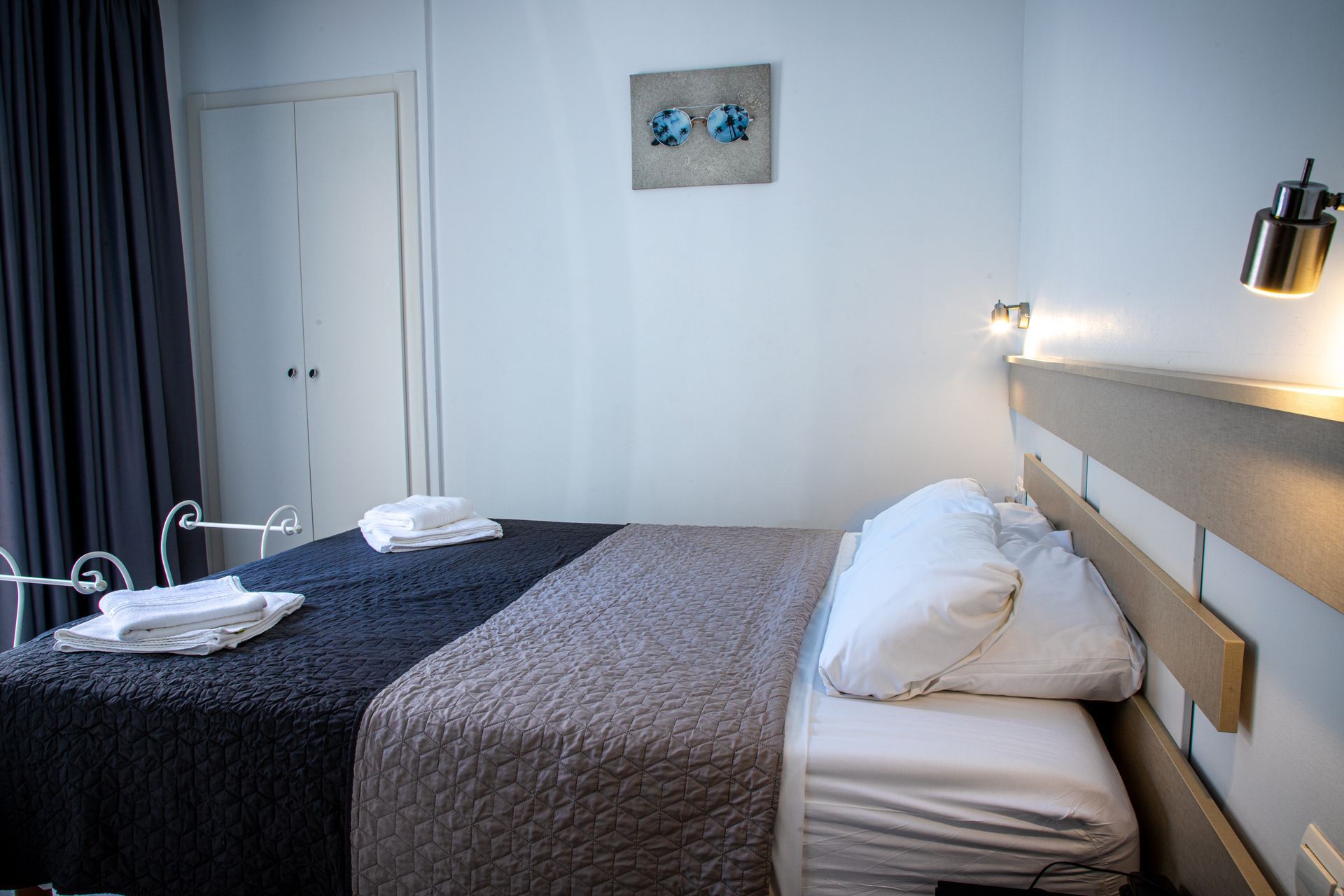 Un dormitorio con una cama doble cubierta con un edredón gris oscuro y beige. Hay toallas blancas sobre la cama.