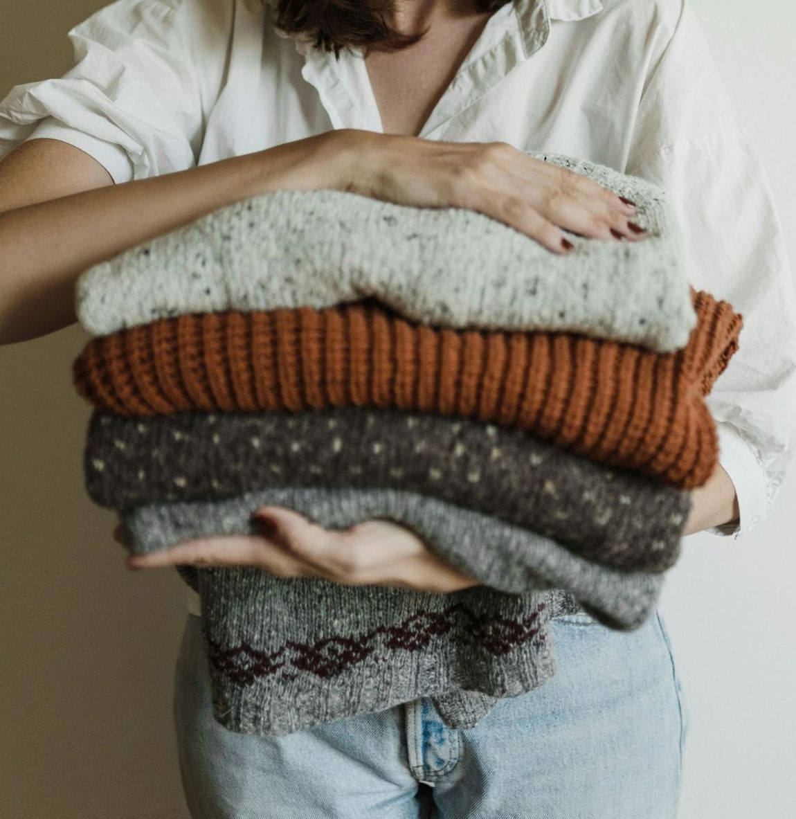 A woman is holding a stack of sweaters in her hands