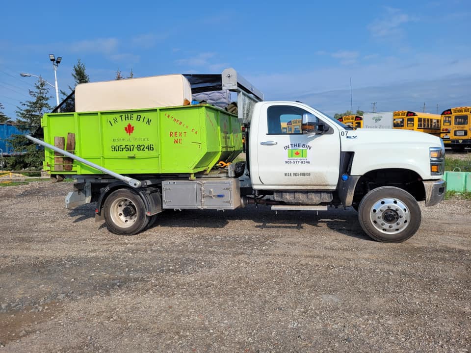 Green and white garbage truck in a parking lot.