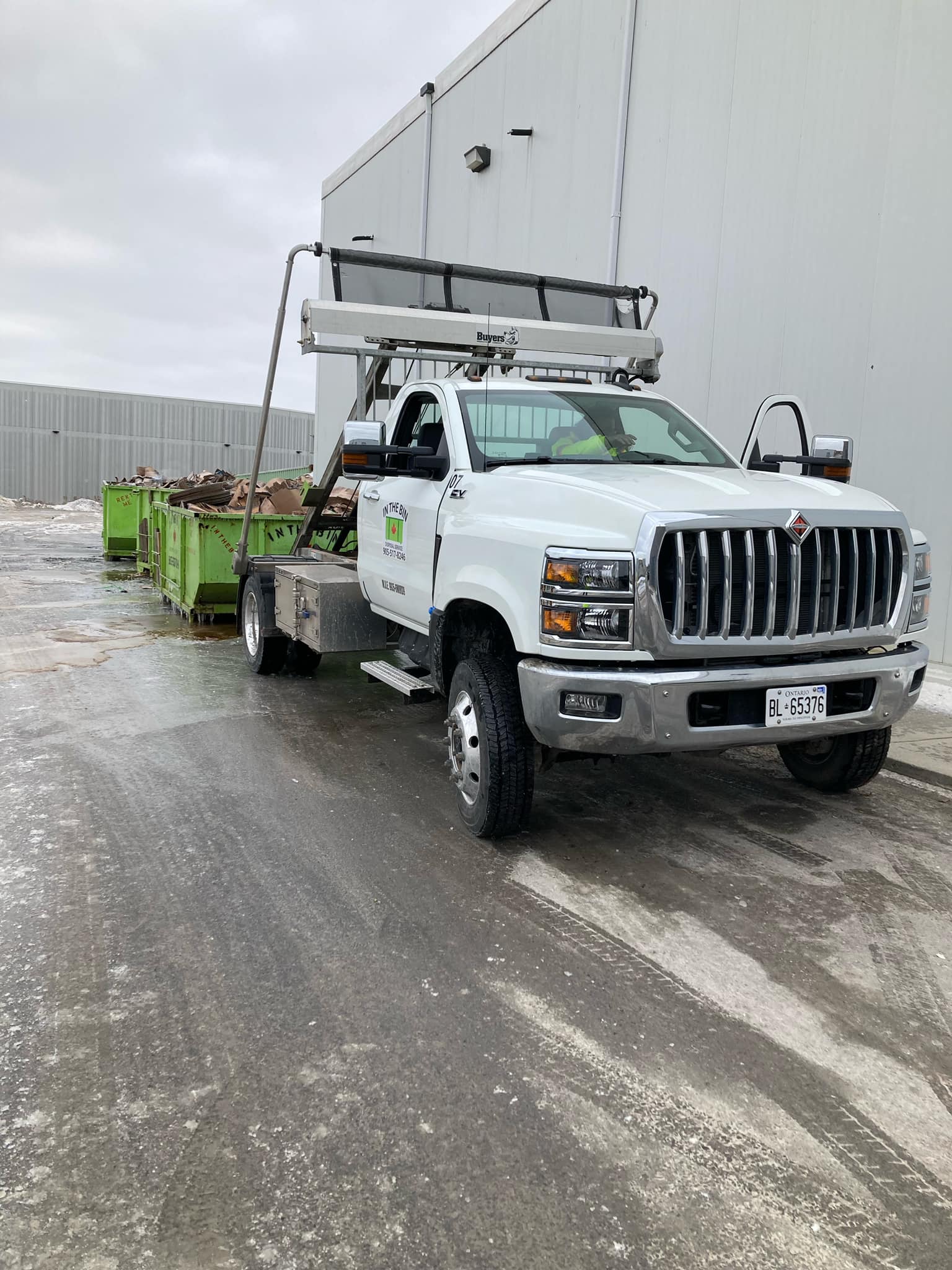 White truck with green dumpster, parked in front of a building.