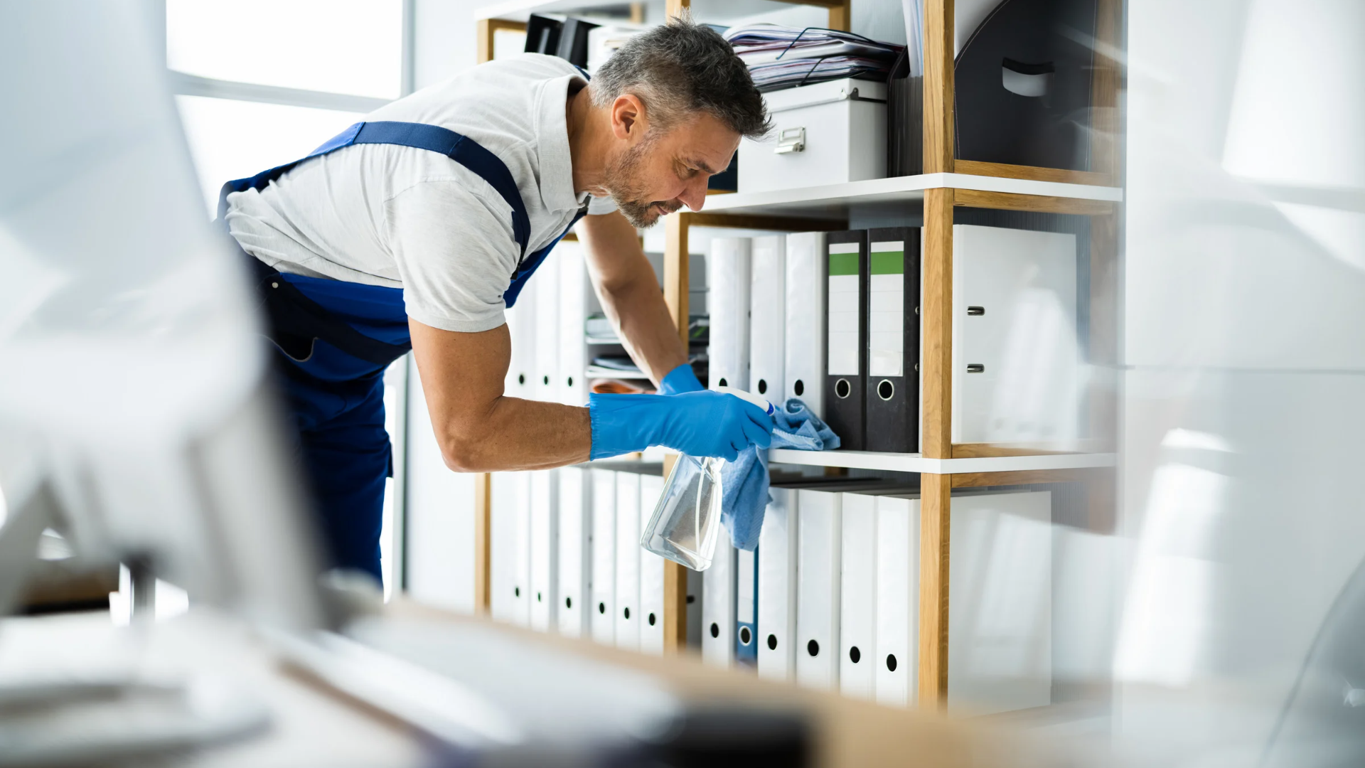 A man is cleaning a shelf with a cloth in an office.
