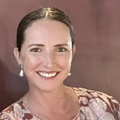 A person with dark hair pulled back, wearing drop earrings and a patterned top, smiles against a solid brownish background.