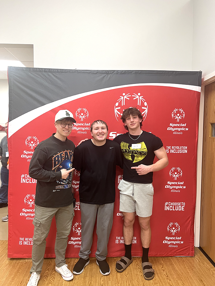 Three people stand smiling in front of a red Special Olympics step-and-repeat backdrop.