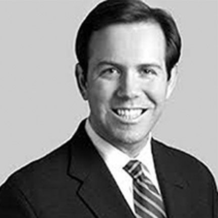 A headshot of a person in a dark suit and striped tie, smiling slightly against a plain, light gray background.