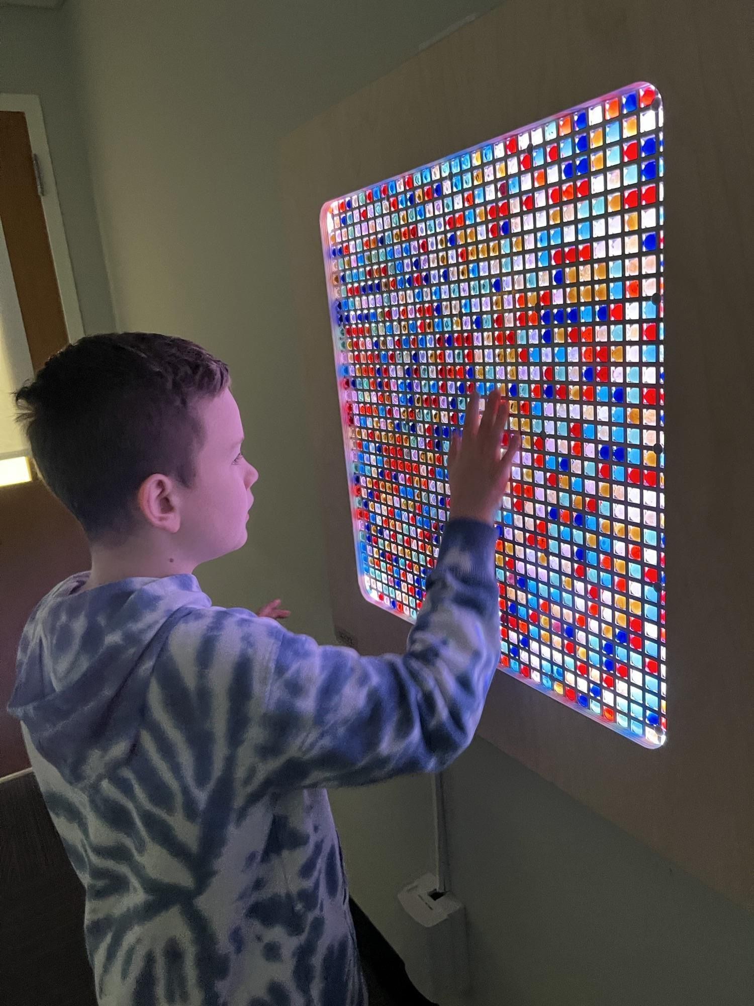 A person touches an interactive light wall made of a grid of blue, red, and yellow translucent tiles.