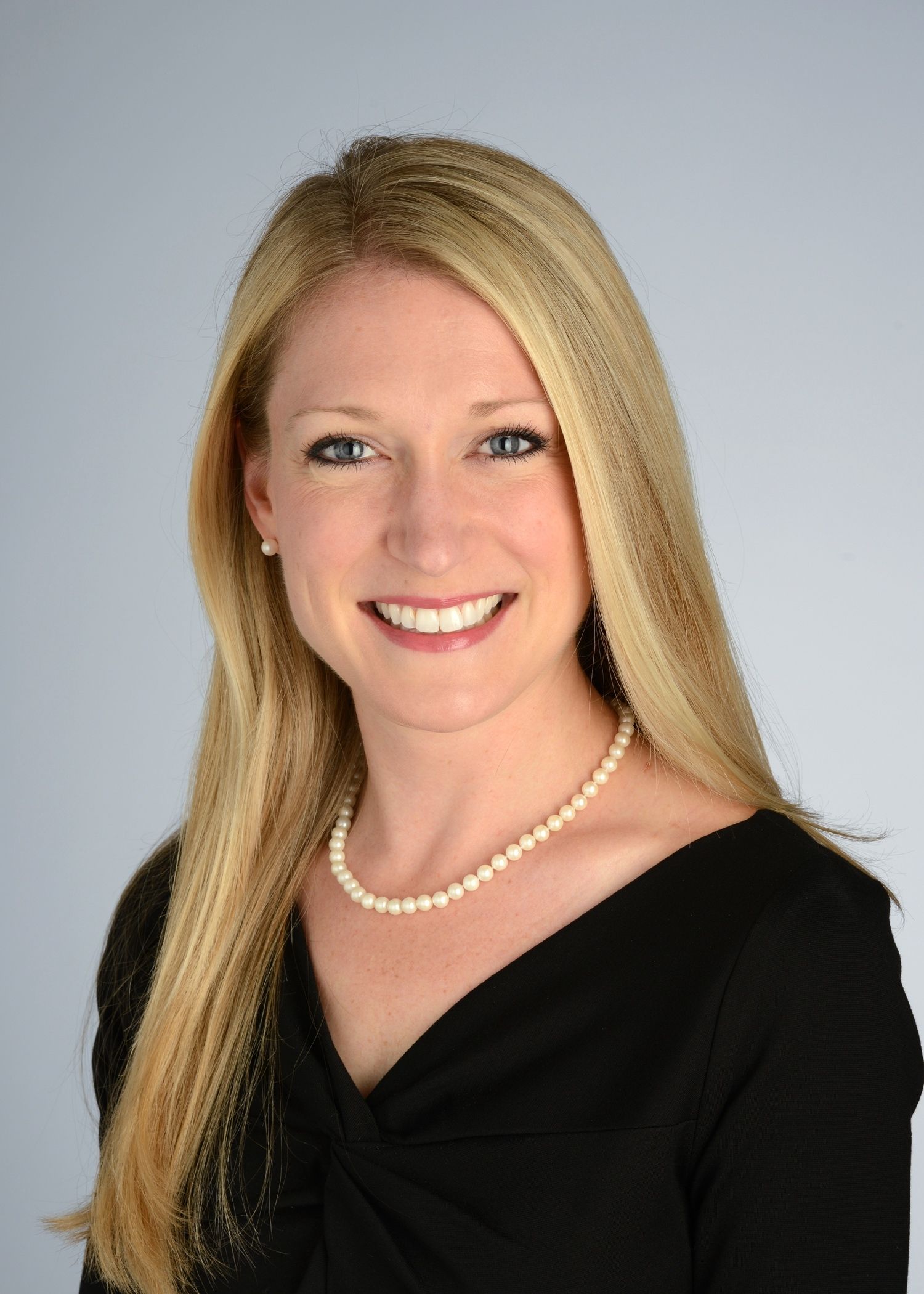 A woman wearing a black shirt and a pearl necklace is smiling for the camera.