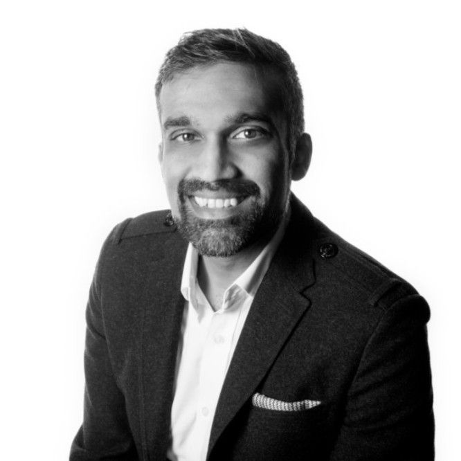 A man with a beard is wearing a suit and smiling in a black and white photo.