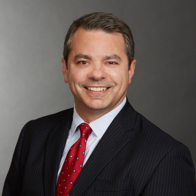 A woman is sitting at a table with her hands folded and smiling.