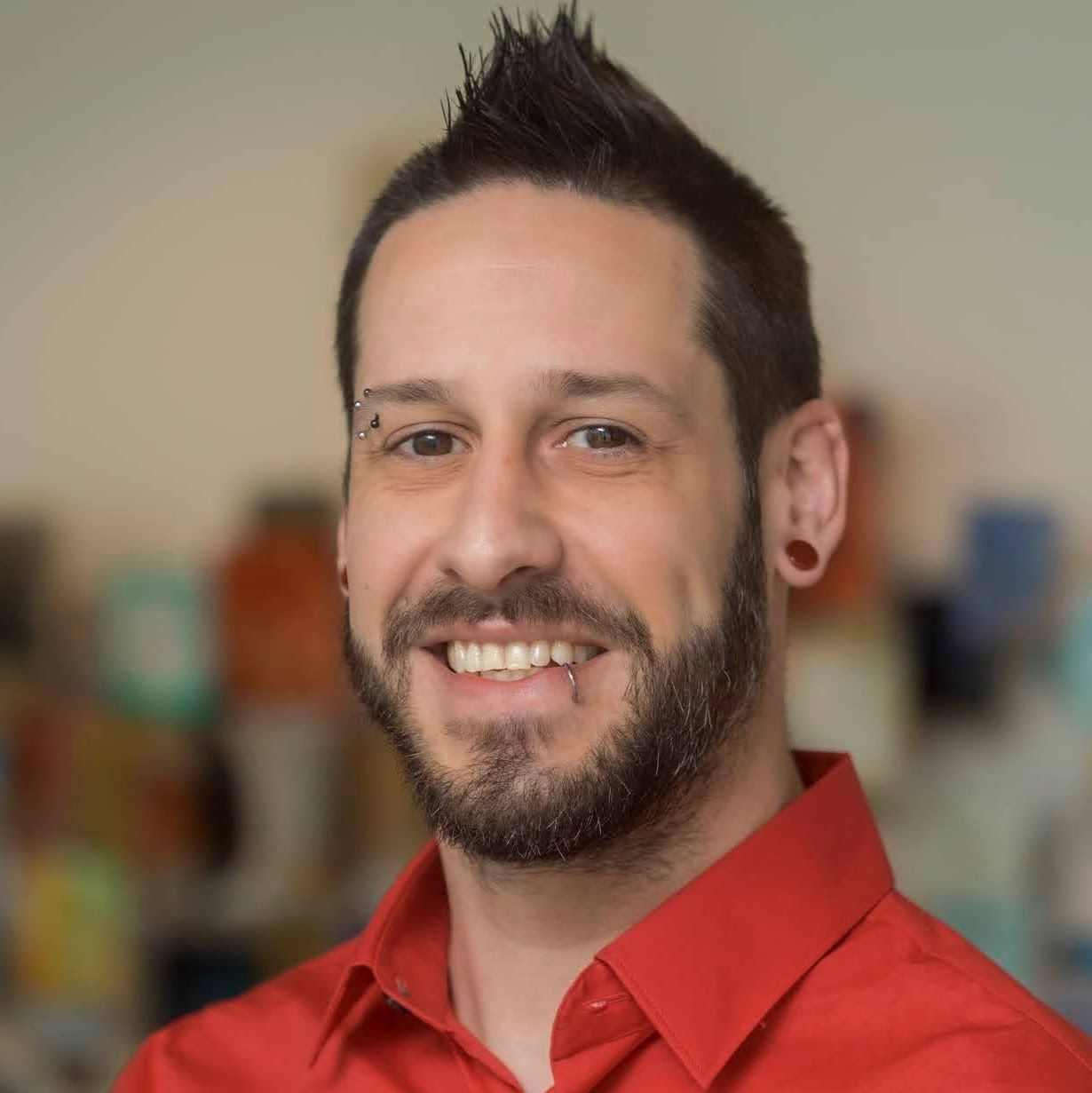 A man with a beard is wearing a red shirt and smiling.