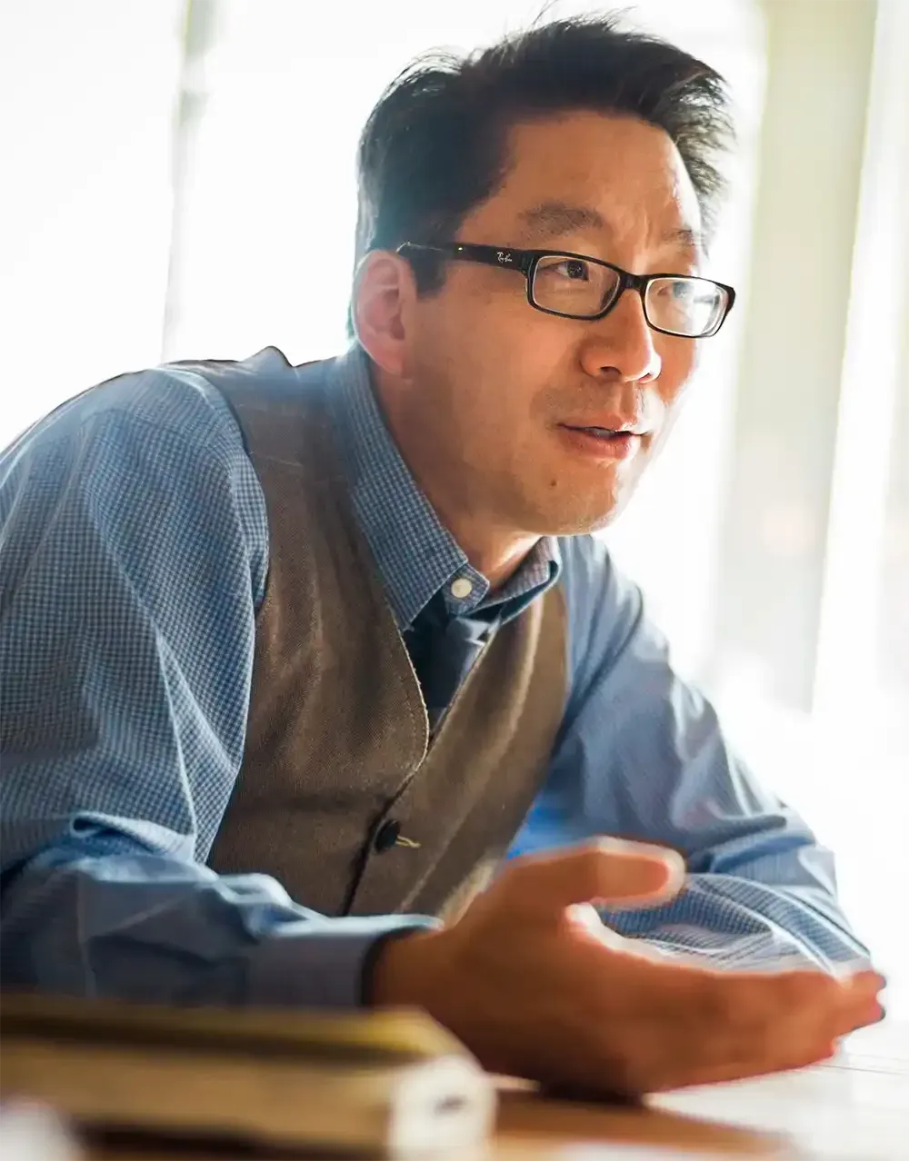 A man wearing glasses and a vest is sitting at a table.