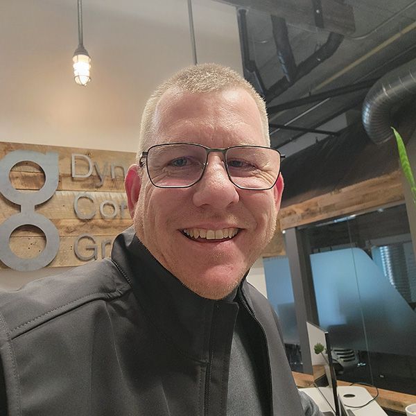 A man wearing glasses and a black vest is smiling for the camera.