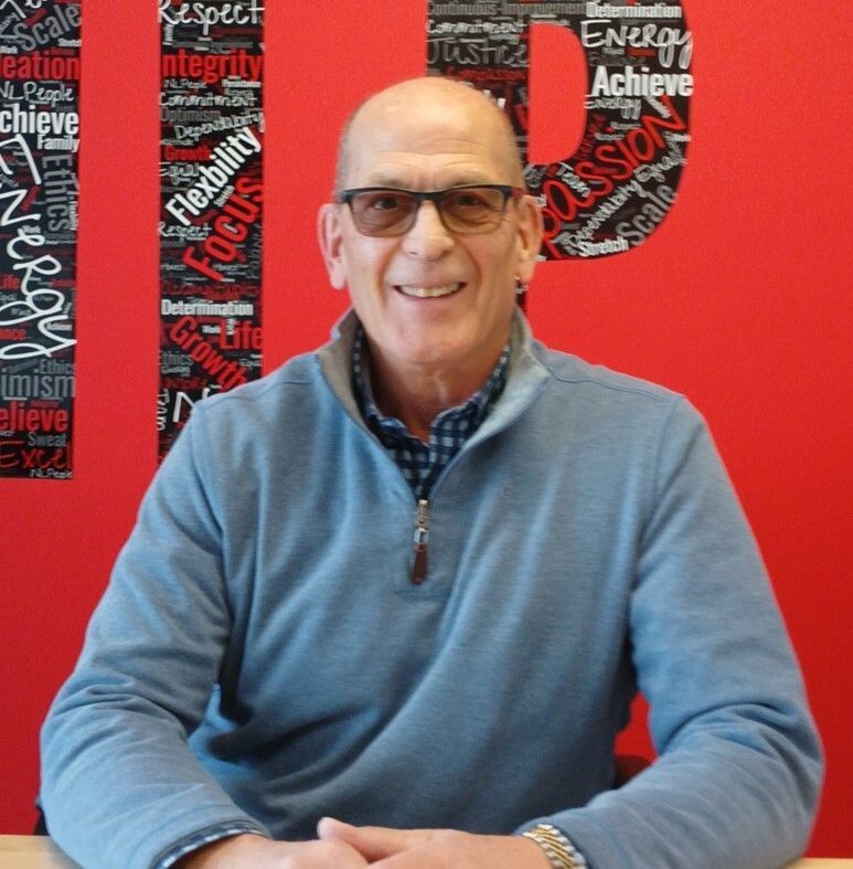 A man in a white shirt is standing with his arms crossed and smiling.