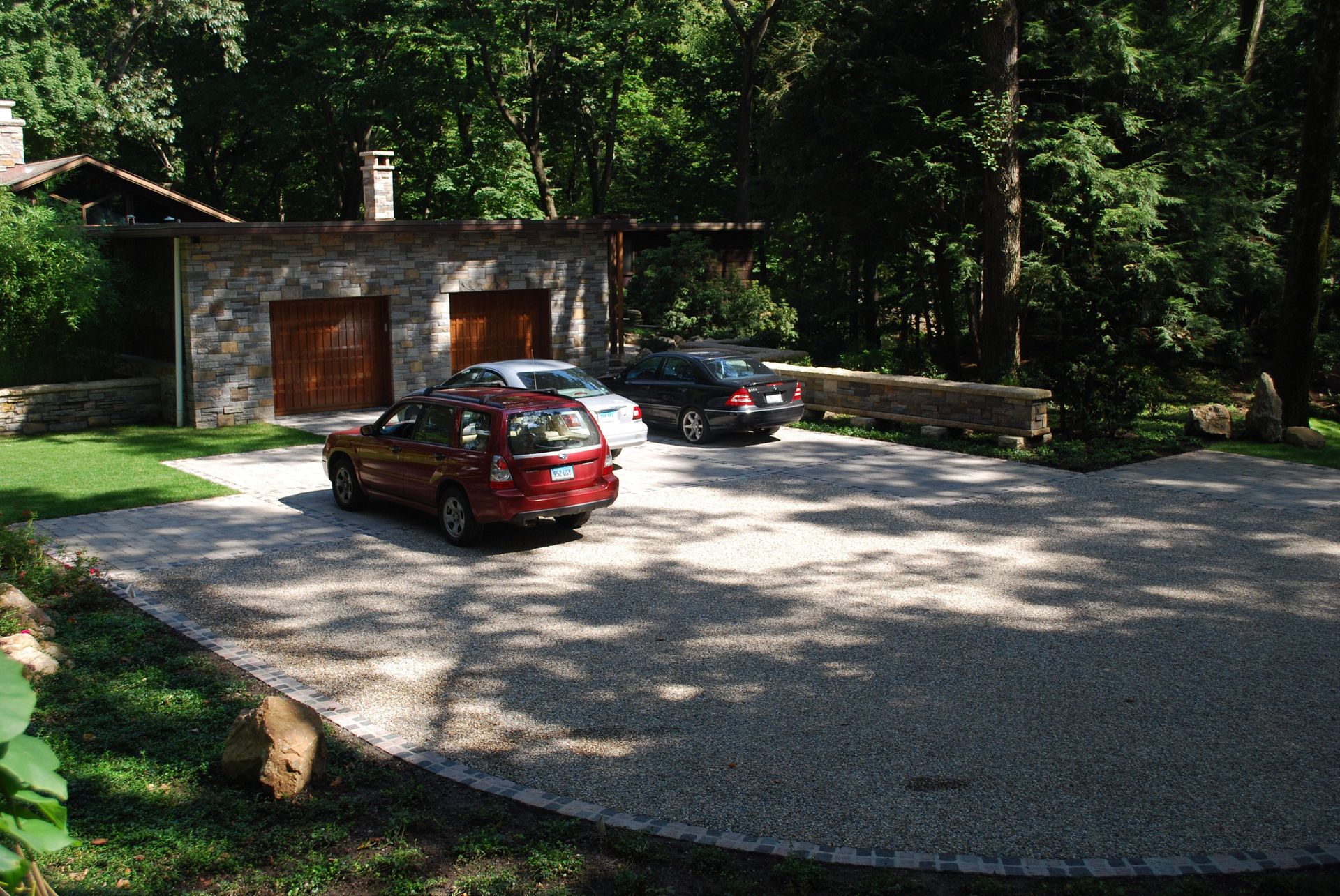 A red car is parked in a gravel driveway in front of a house