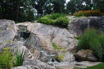 A waterfall is surrounded by rocks and trees in a park.