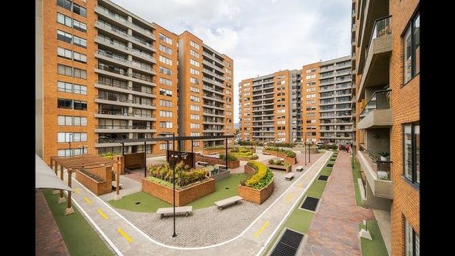 Patio de complejo de apartamentos con edificios de ladrillo, pasarelas, espacios verdes y bancos.