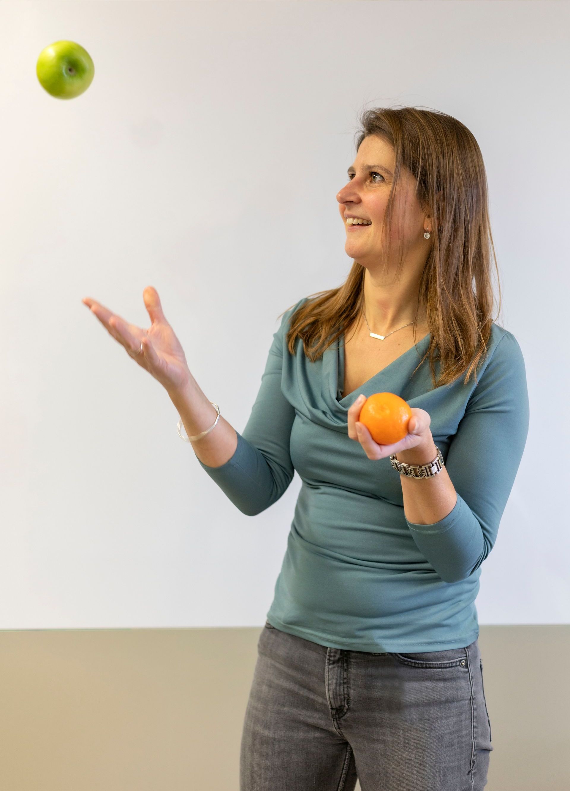 Een persoon die lacht terwijl zij jongleert met een groene appel en een sinaasappel.