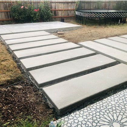 A concrete walkway in a backyard with a trampoline in the background.