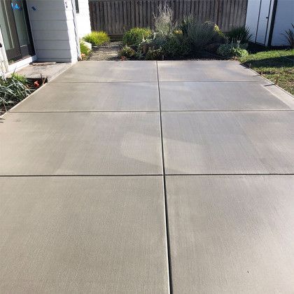 A concrete driveway in front of a house with a fence in the background.