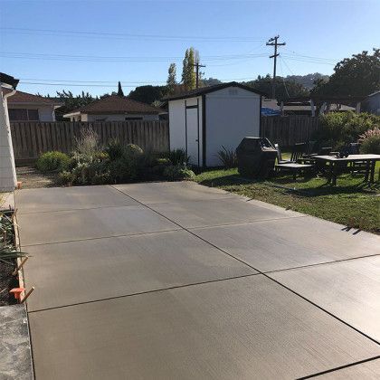 There is a large concrete driveway in the backyard of a house.