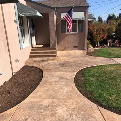 A concrete walkway leading to a house with an american flag in front of it.
