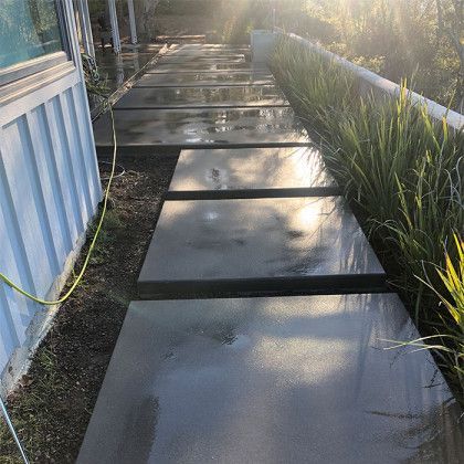 A concrete walkway leading to a house with a hose attached to it.