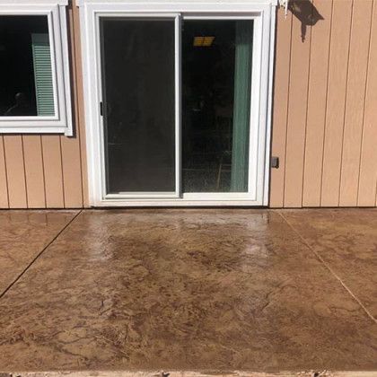 A concrete patio with a sliding glass door in front of a house.