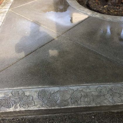 A concrete walkway with a planter in the background and a reflection of a person in the water.