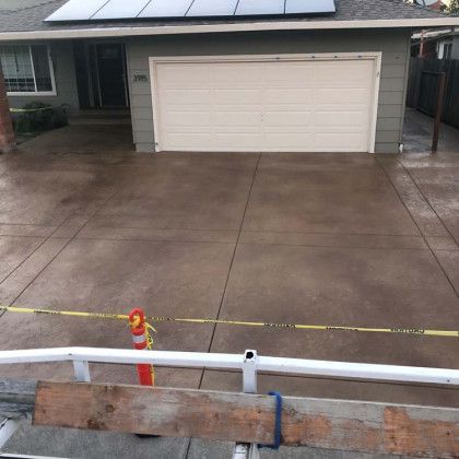 A concrete driveway in front of a house with a solar panel on the roof.