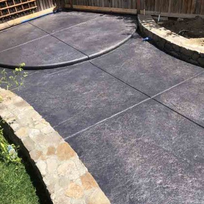 A concrete patio with a stone wall and a fence in the background.