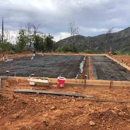 A concrete foundation is being built in a dirt field with mountains in the background.