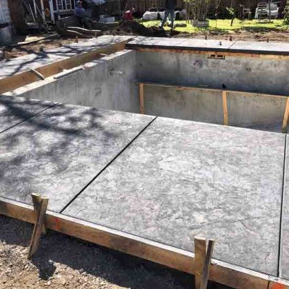 A large concrete pool is being built in a backyard.