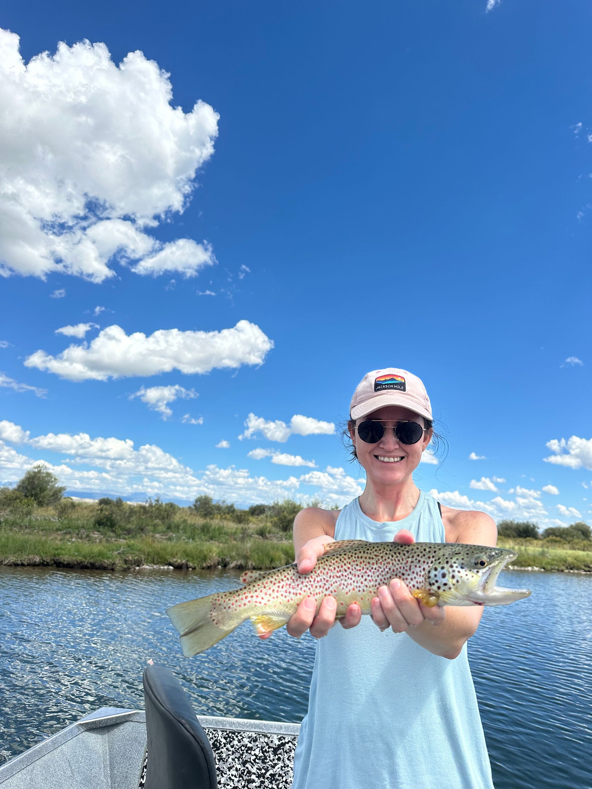 A woman is holding a brown trout on a boat.