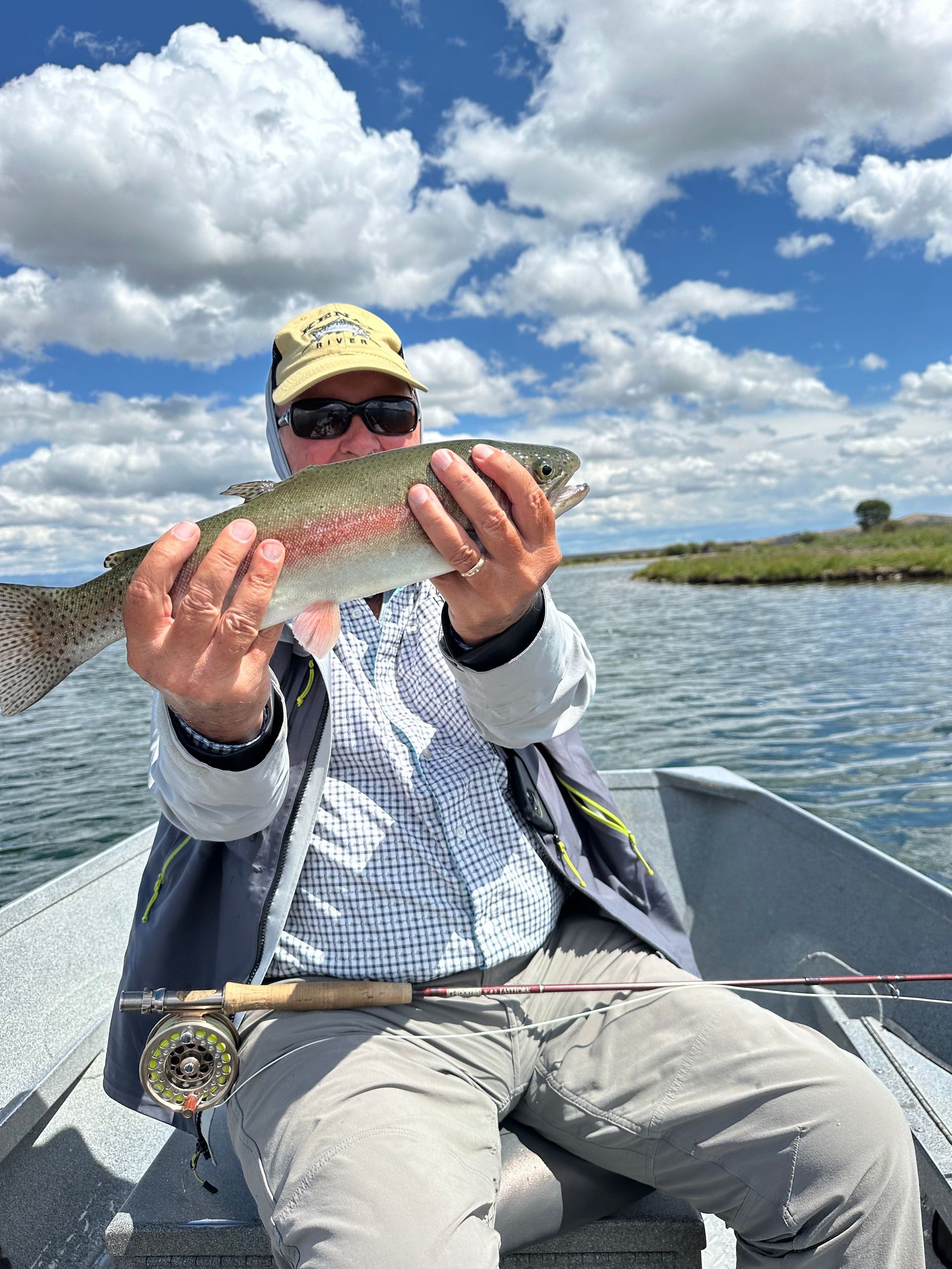 A man is sitting in a boat holding a rainbow trout.
