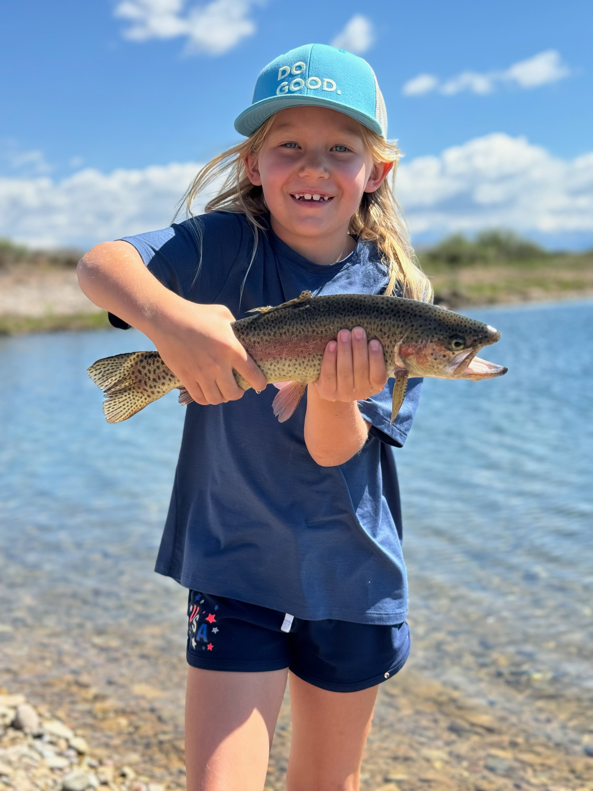 A little girl is holding a rainbow trout in her hands.