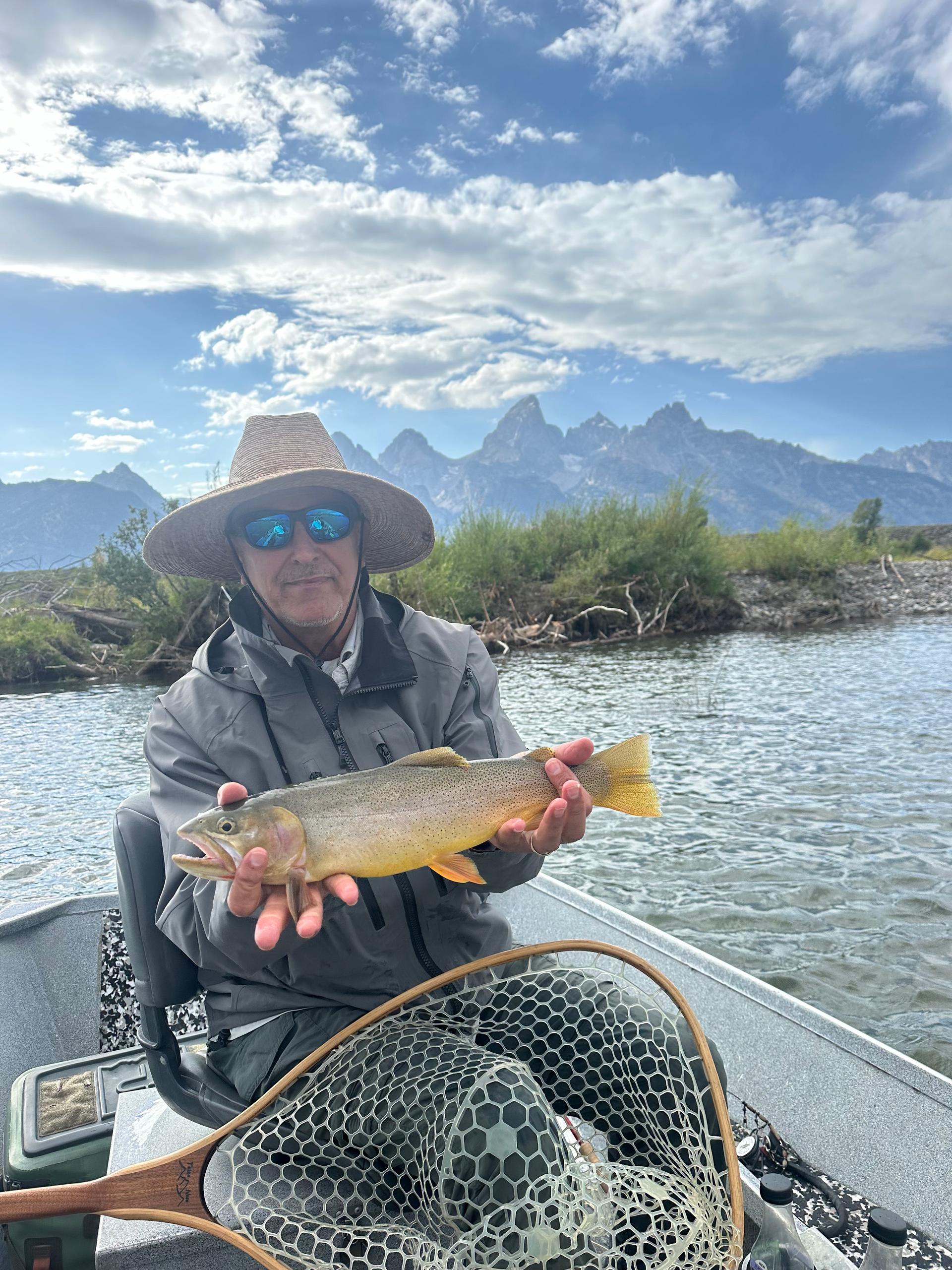 A man is sitting on a boat holding a brown trout.