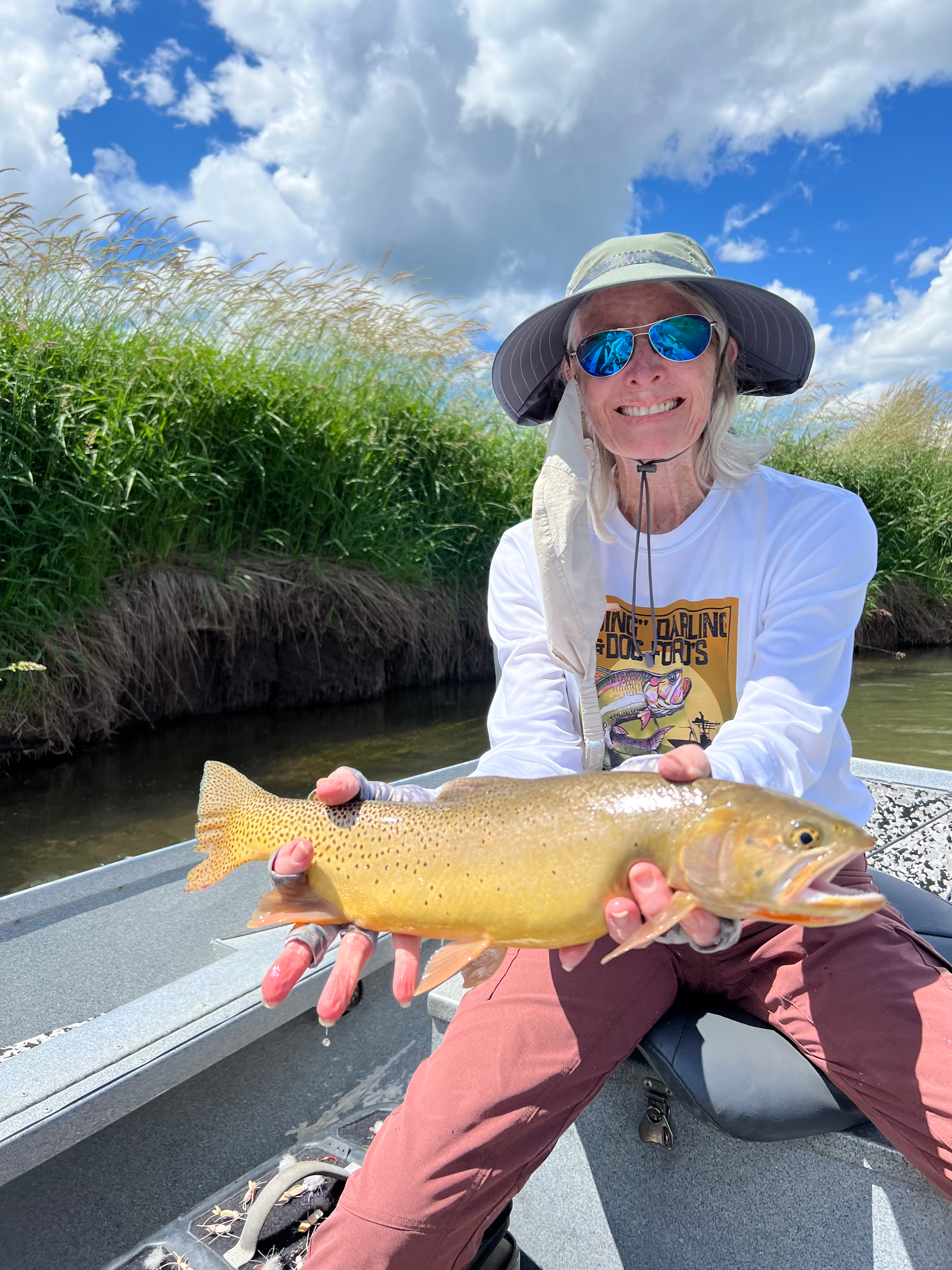 A woman is sitting on a boat holding a brown trout.
