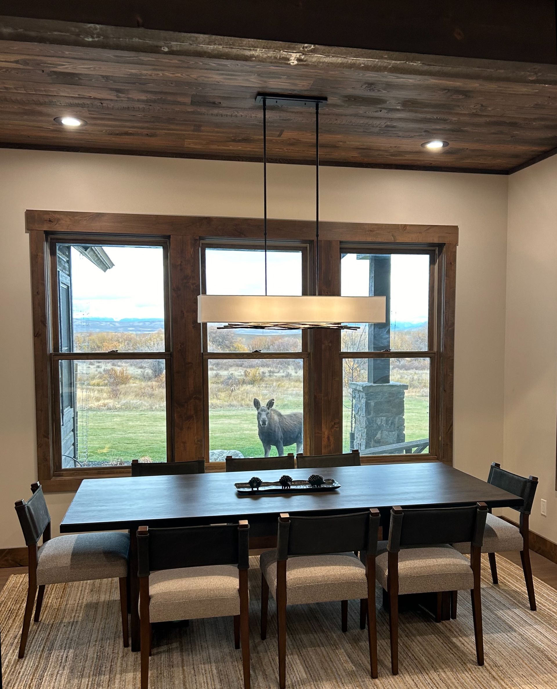 A dining room with a table and chairs and a rhino in the window.