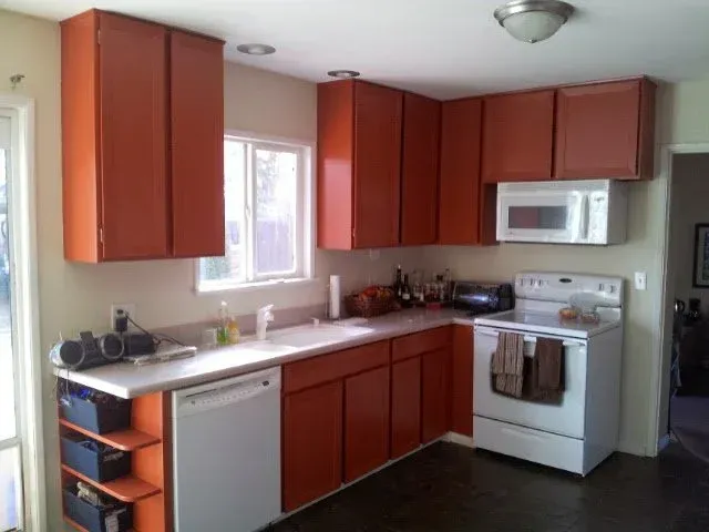 Orange kitchen cabinets in a kitchen with a white dishwasher, stove, and microwave.