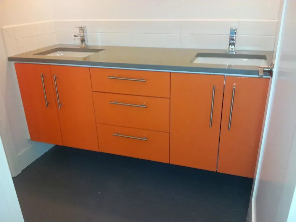 Orange bathroom vanity with two sinks, gray countertop, and silver hardware. Dark floor.