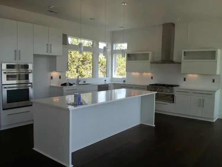 Modern white kitchen with island, stainless steel appliances, and dark wood floors.