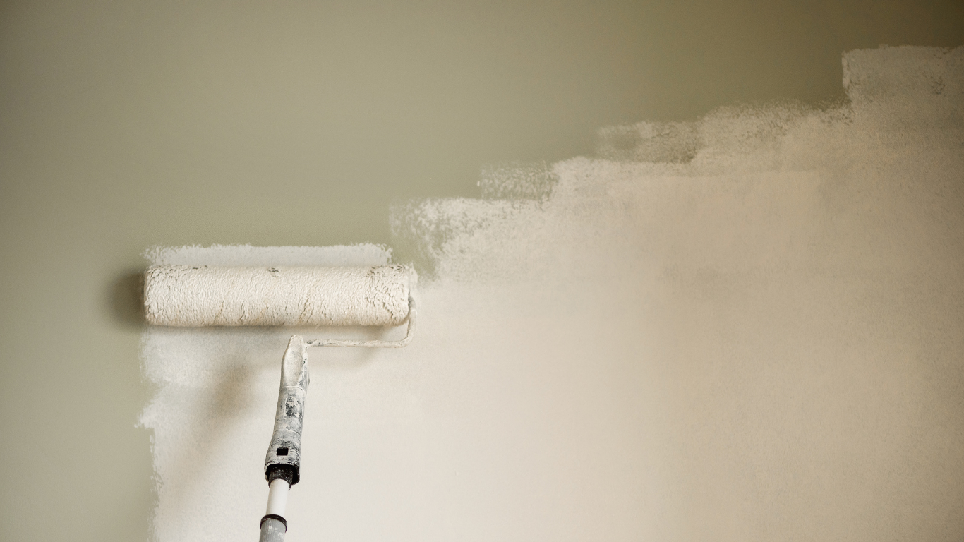 A paint roller painting a beige wall white.