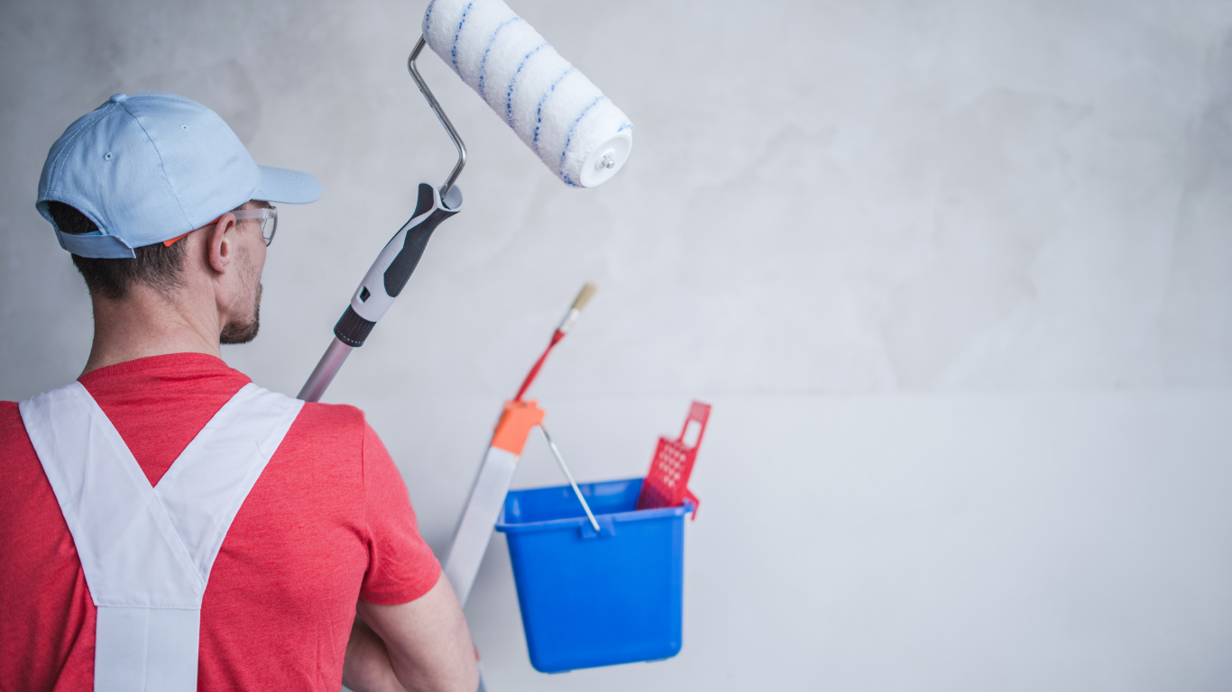 Painter holding roller and bucket, painting white wall.