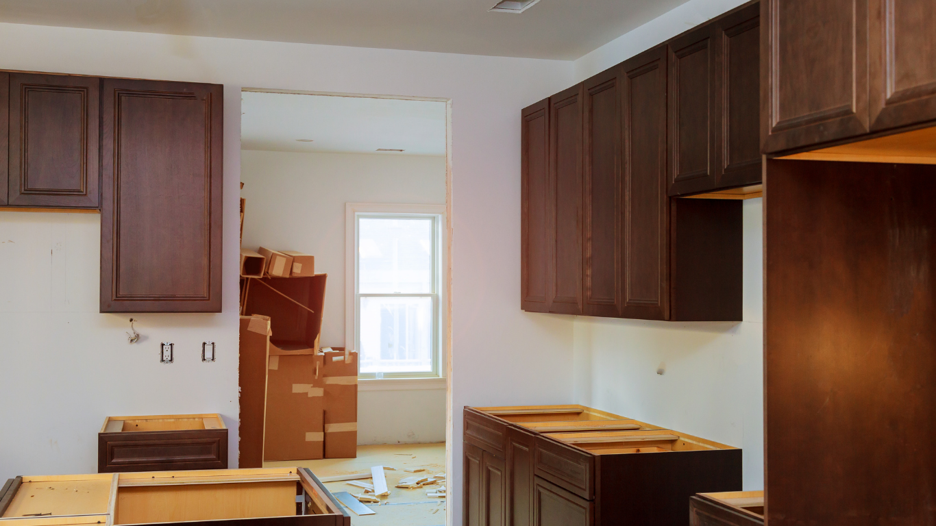 Kitchen renovation in progress, dark brown cabinets installed against white walls, view into a room with boxes.