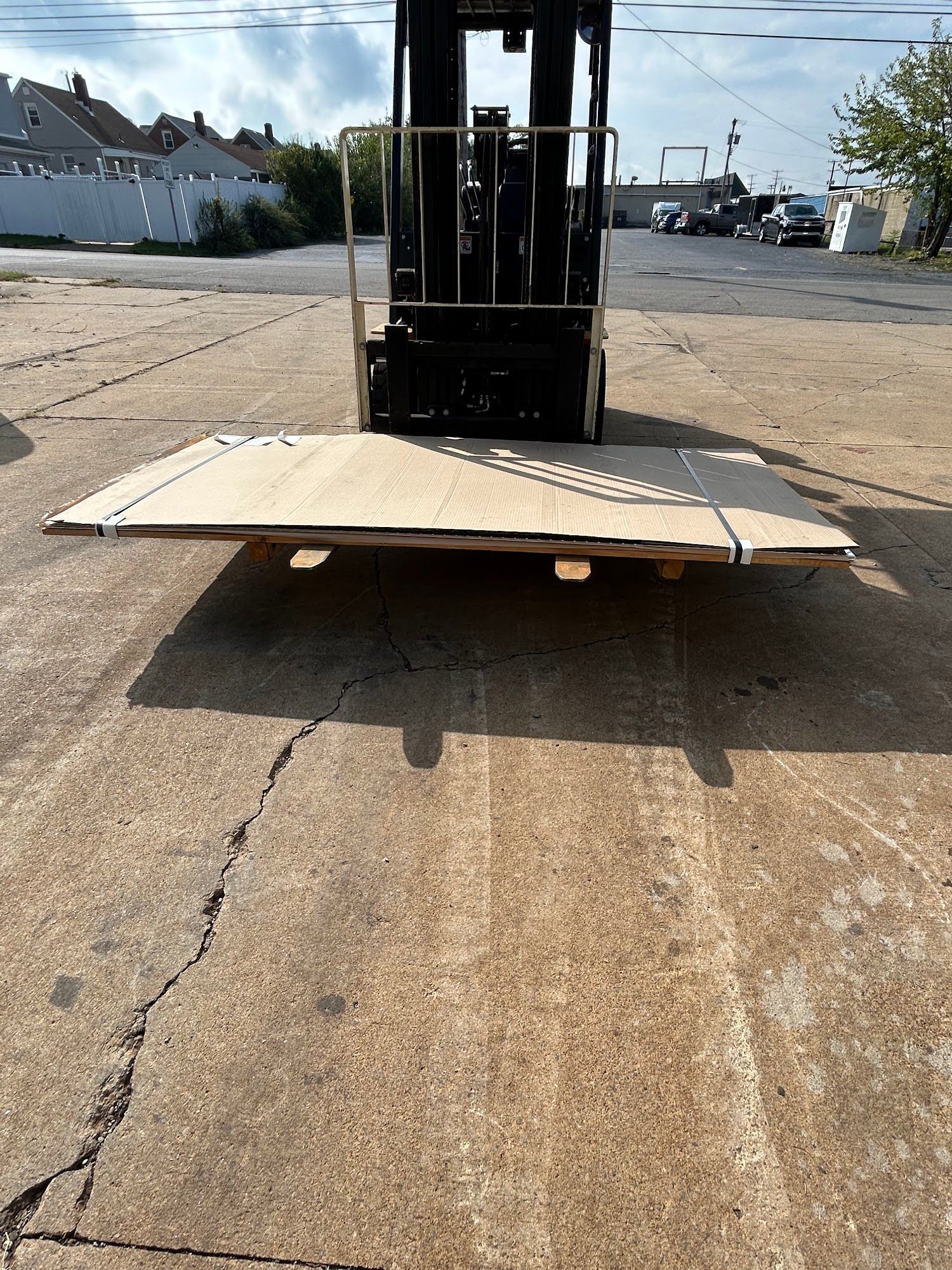 Forklift lifting a large, light-colored wooden platform on a cracked, gray asphalt surface outdoors.