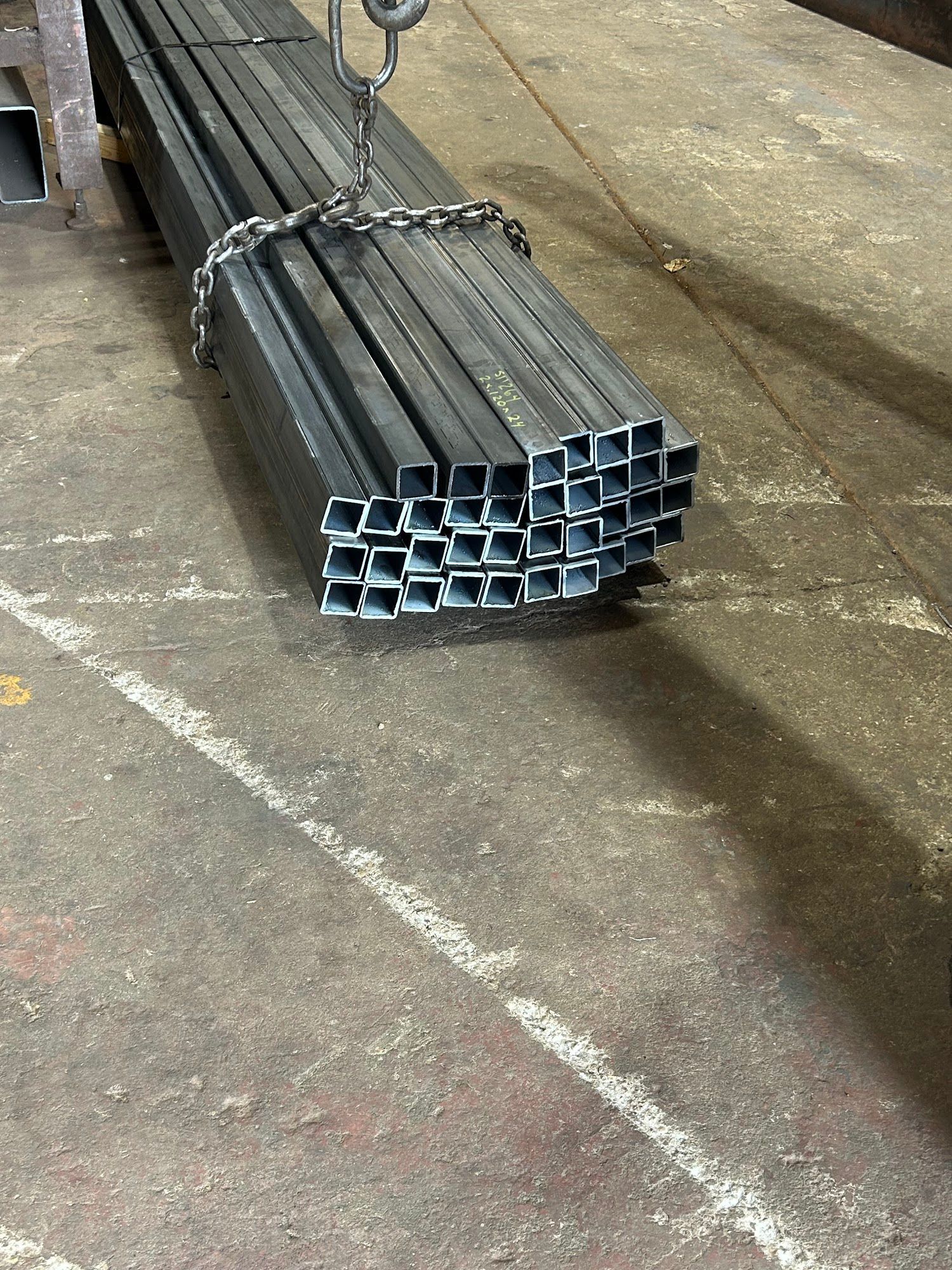 Bundle of square metal tubes suspended by a chain and hook.